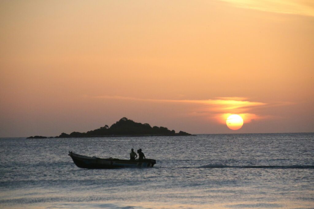 A serene sunset over Negombo, Sri Lanka, with a boat silhouetted on the ocean.